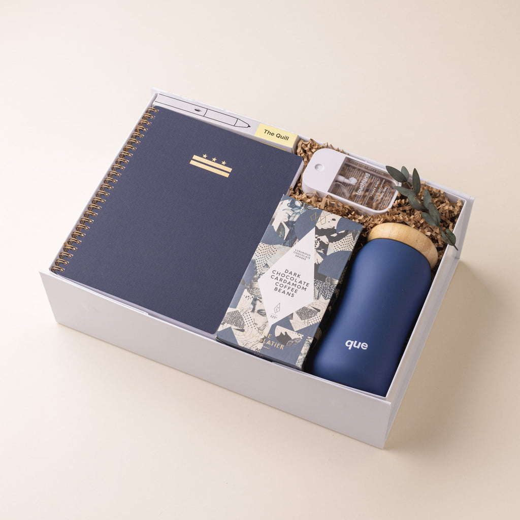 Modern home office gift box with notebook, pen, water bottle, hand sanitizer and chocolate covered coffee beans.