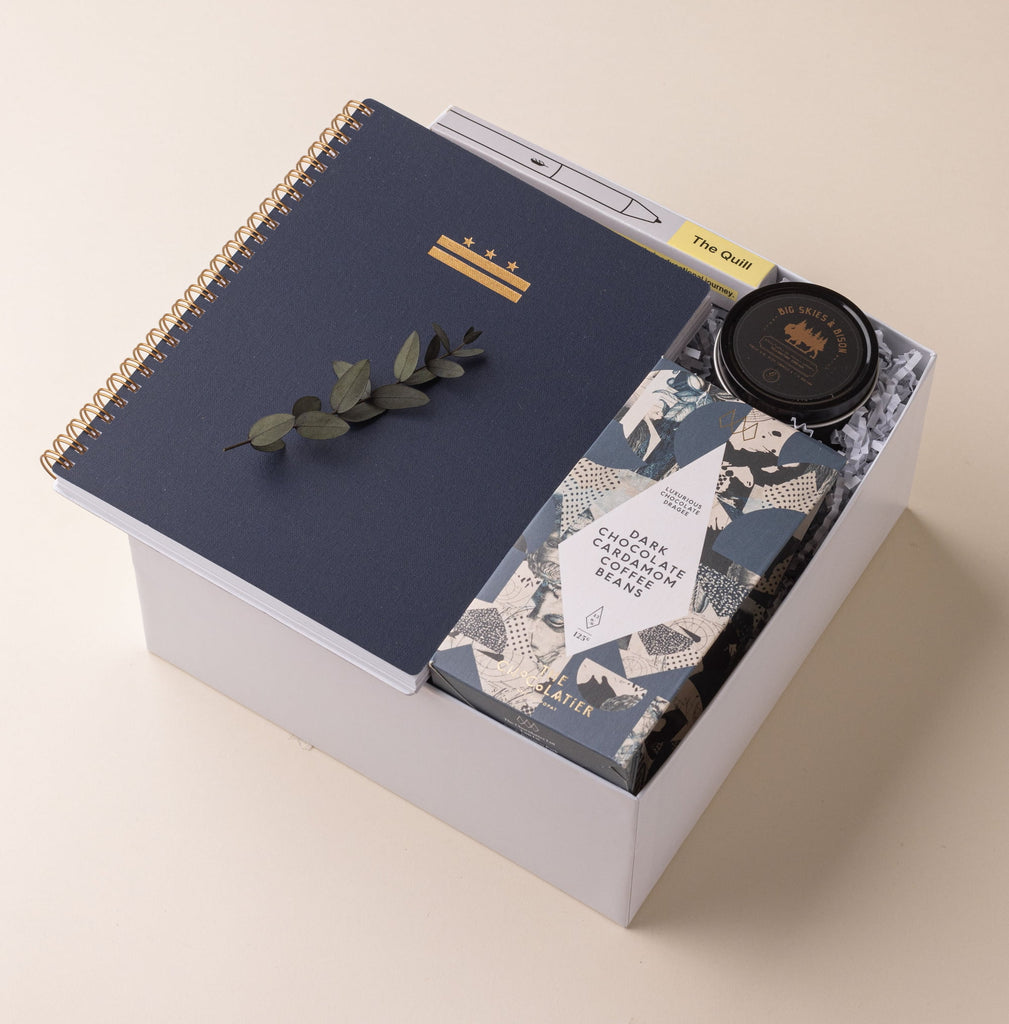 Modern gender neutral office gift box with notebook, pen, chocolate coffee beans and travel candle.