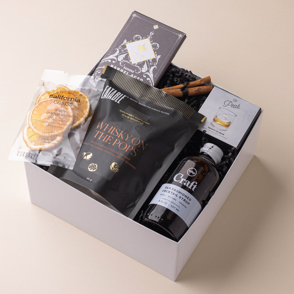 Modern whiskey gift set with crispy orange slices, Whiskey On The Pops popcorn by EATABLE, choice of cocktail mixer by W&P, Peak ice cube mold by W&P, and bourbon chocolate bar by Harper Macaw.
